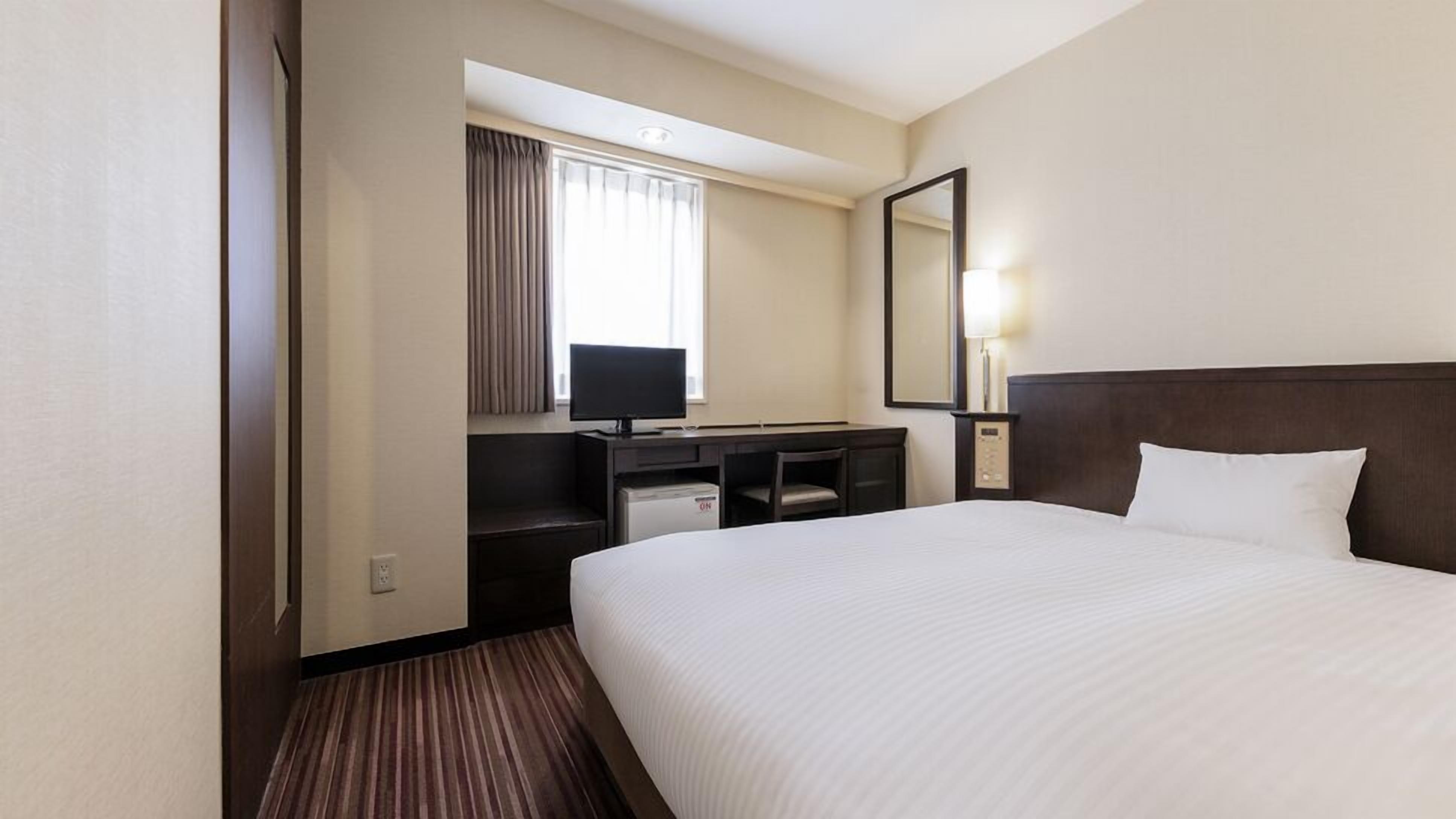 A hotel room with a bed, a desk with a computer, a television, and a mirror.
