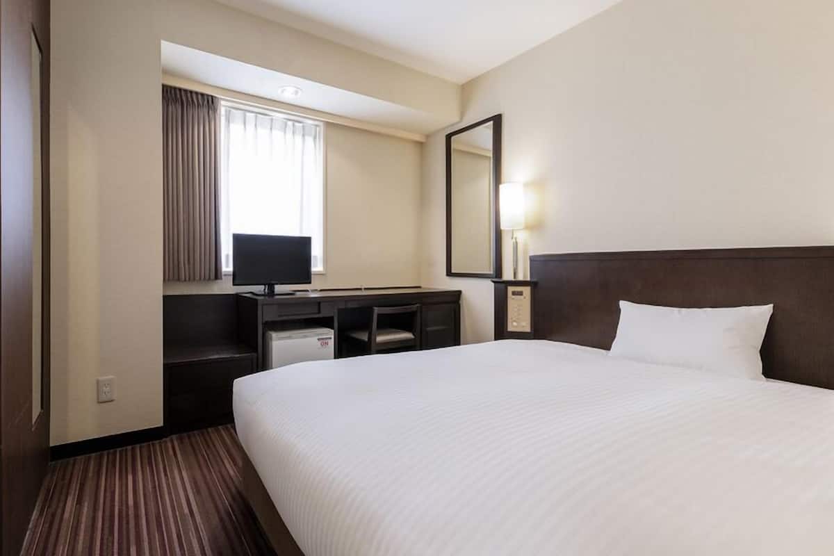 A hotel room with a bed, a desk with a computer, a television, and a mirror.