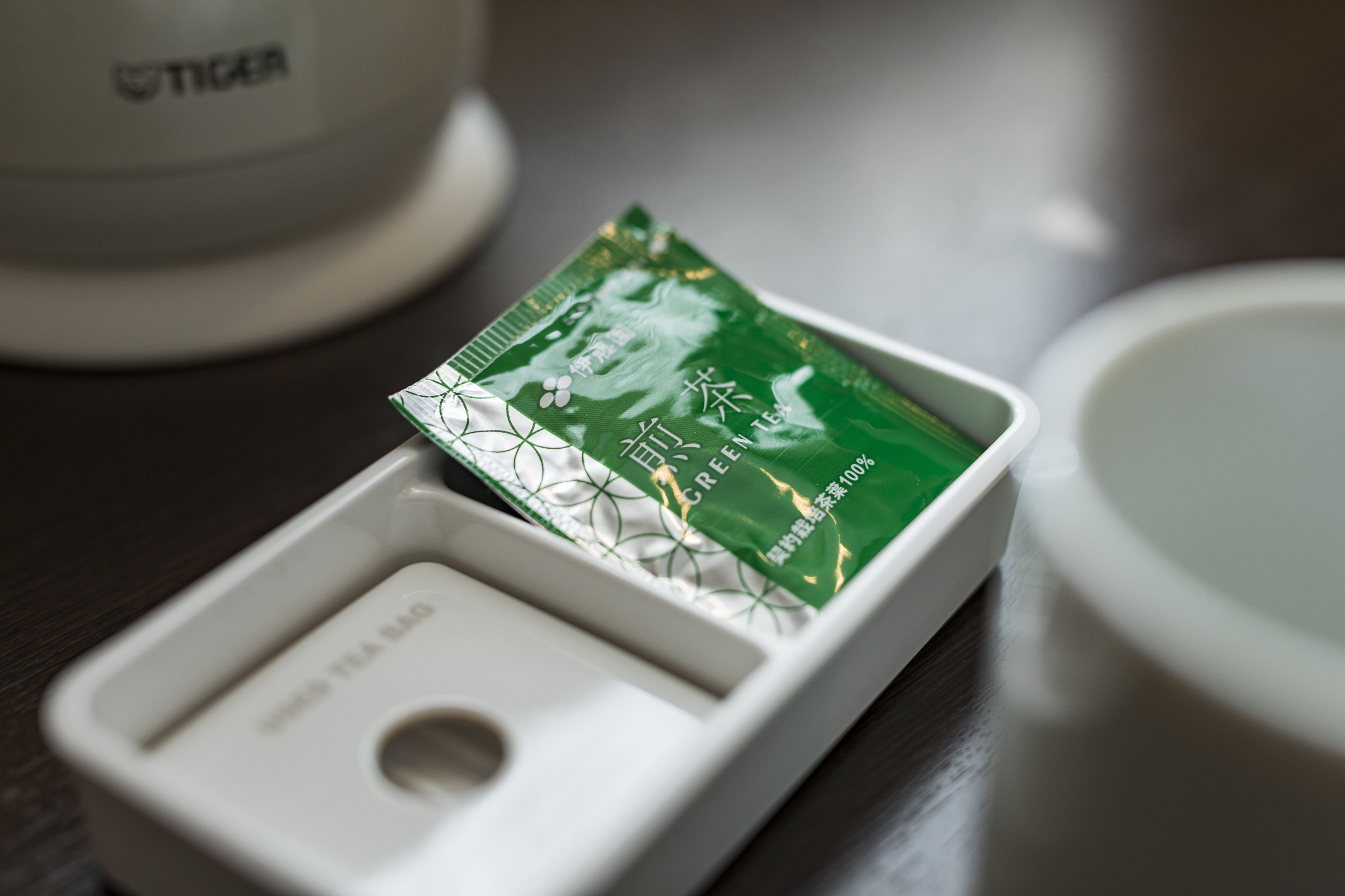 A white tea bag container with a green tea bag partially visible.