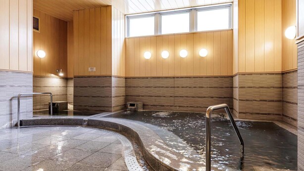 Un onsen japonais traditionnel, avec des panneaux de bois, un bain en pierre et un sol carrelé.