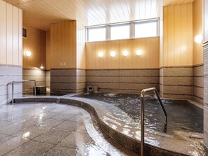 Een traditionele Japanse onsen met houten lambrisering, een stenen bad en een betegelde vloer.