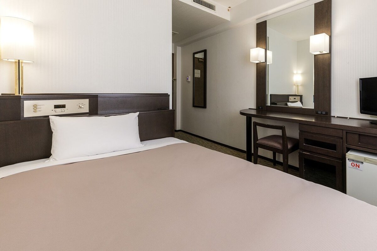 A hotel room with a bed, a desk, a television, and a mirror.