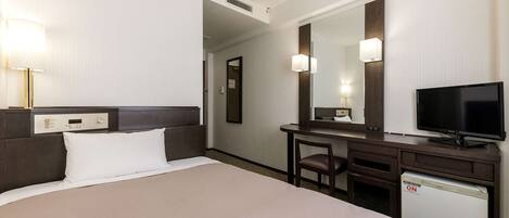 Quarto de hotel com uma cama, uma escrivaninha com televisão, uma cadeira e um pequeno frigorífico.