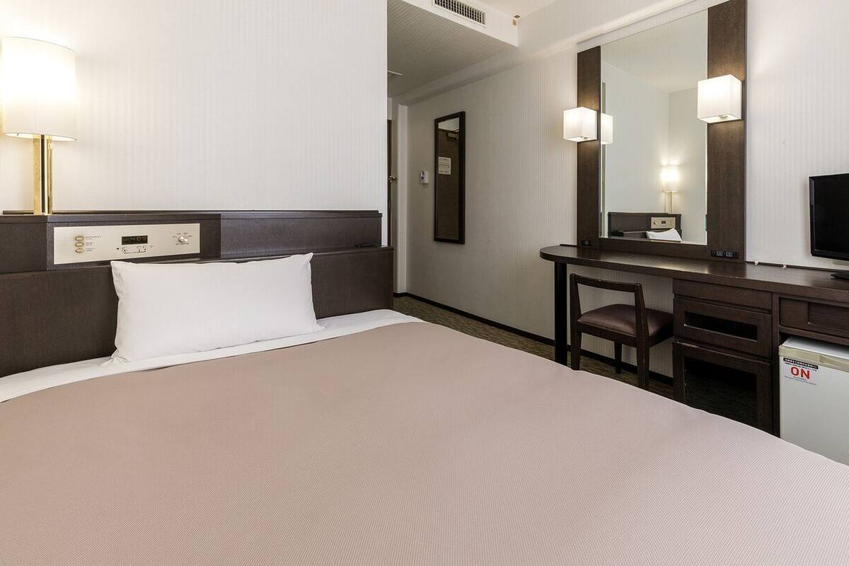 A hotel room with a bed, a desk, a television, and a mirror.