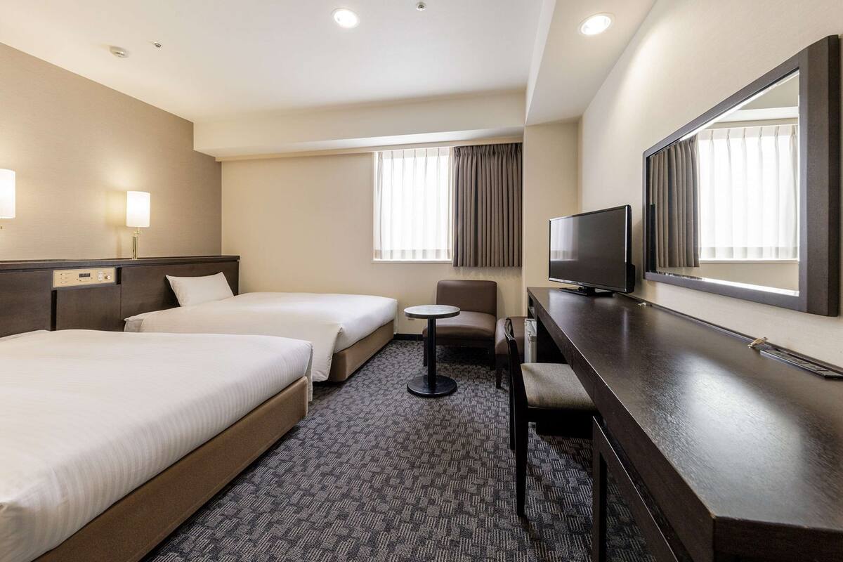 A hotel room with two beds, a desk, a chair, a television, and a large mirror.