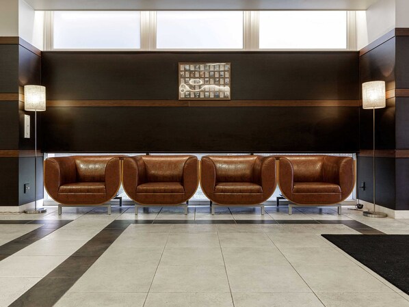 A lobby with four leather armchairs, a dark wall with a framed picture, and two floor lamps.