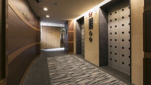 Un couloir d’hôtel doté d’un sol recouvert de moquette, de murs en bois et de deux ascenseurs au design moderne.