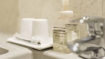 A bathroom with a white sink, a bottle of face and hand foam, and a paper towel dispenser.