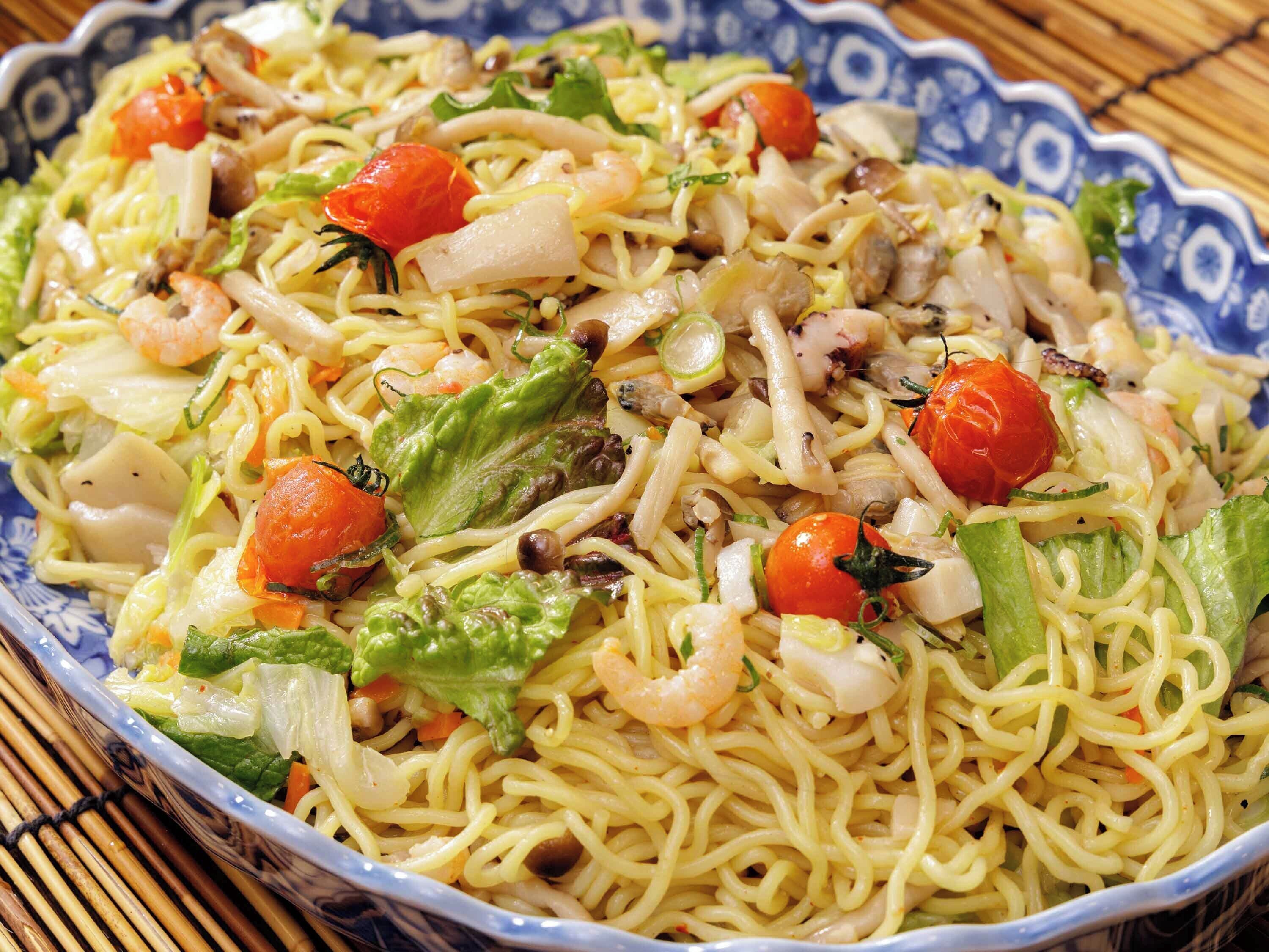 A bowl of pasta with shrimp, vegetables, and a blue patterned bowl.