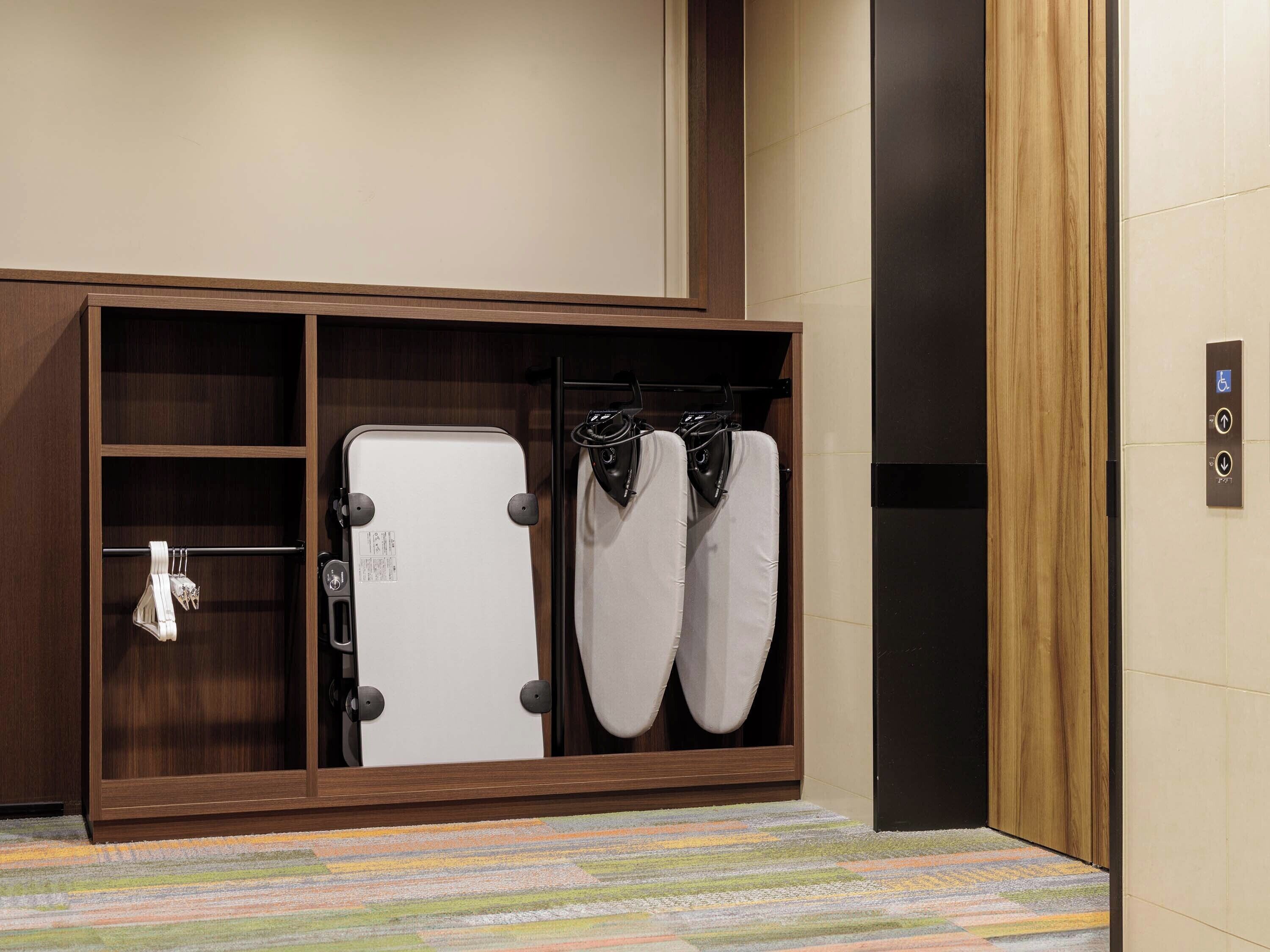 A hotel room with a wooden wardrobe, a white suitcase, and a black handbag hanging on hooks.