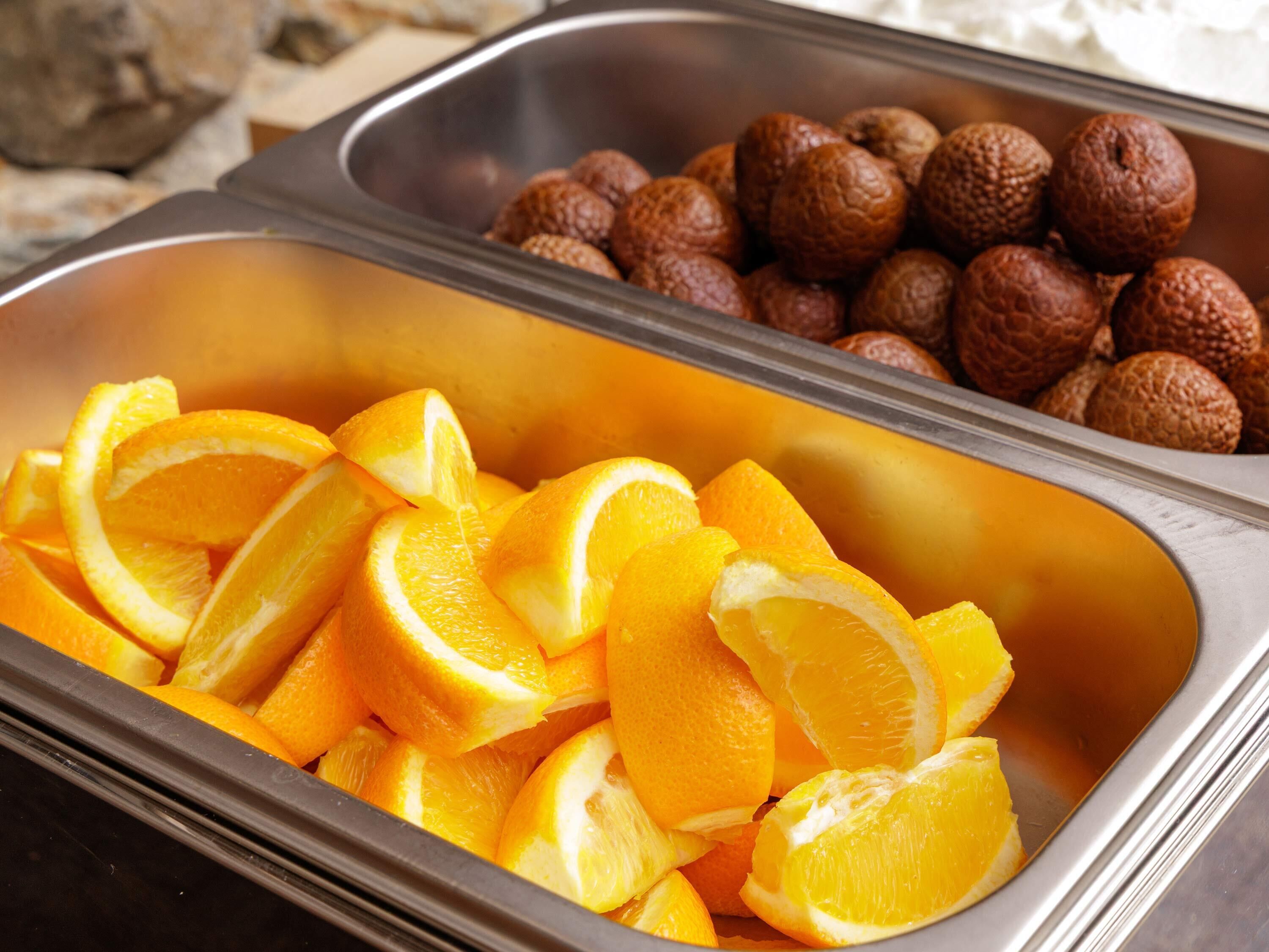 A buffet with sliced oranges and round, brown snacks in metal containers.
