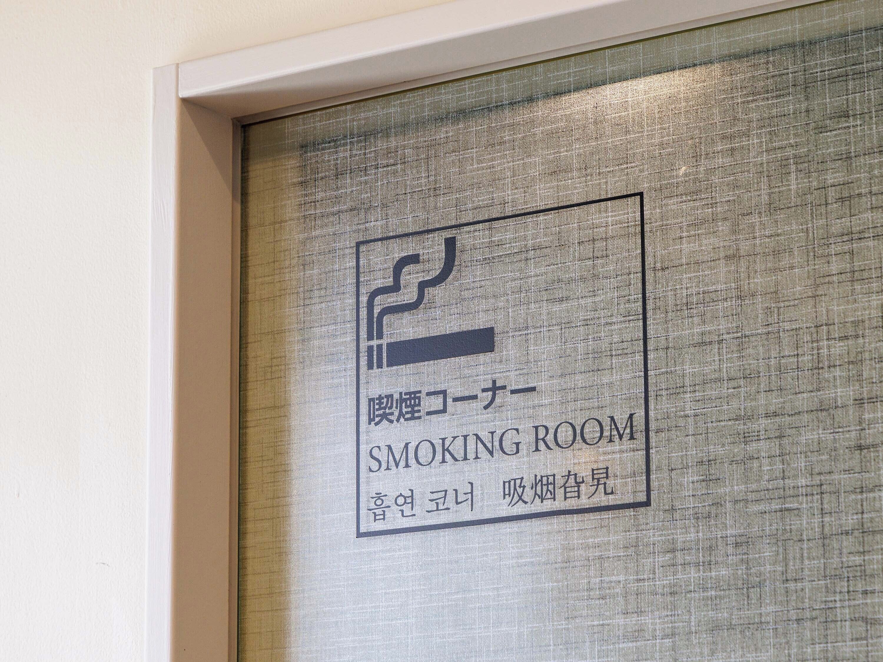 Indicador que mostra una sala per fumar, amb un logotip i text en anglès i un altre idioma.