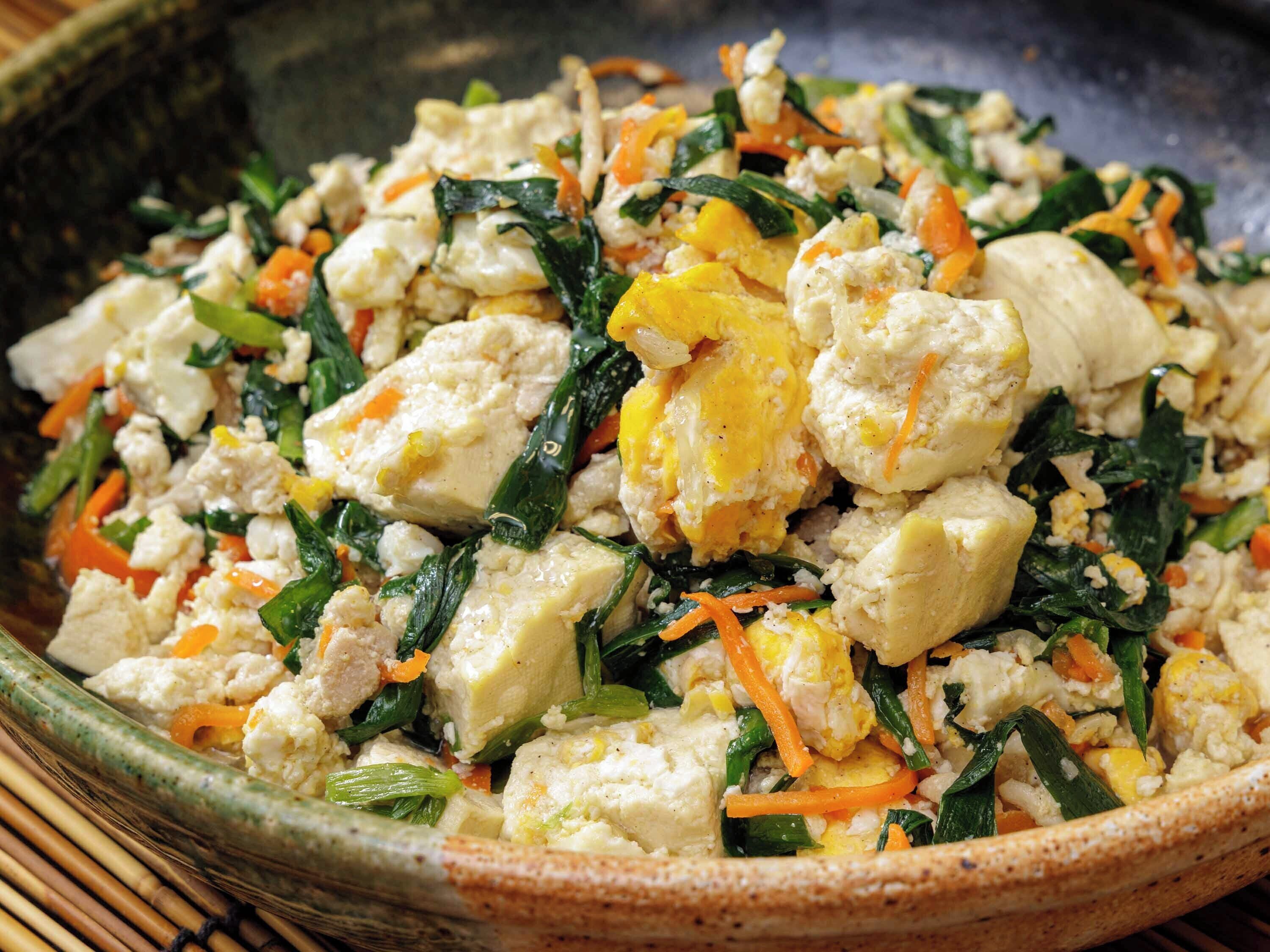 A close-up of a dish with tofu, carrots, and greens in a ceramic bowl.