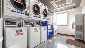 Une laverie équipée de plusieurs machines à laver et de plusieurs séchoirs, ainsi que d’un distributeur automatique et d’un point d’eau.
