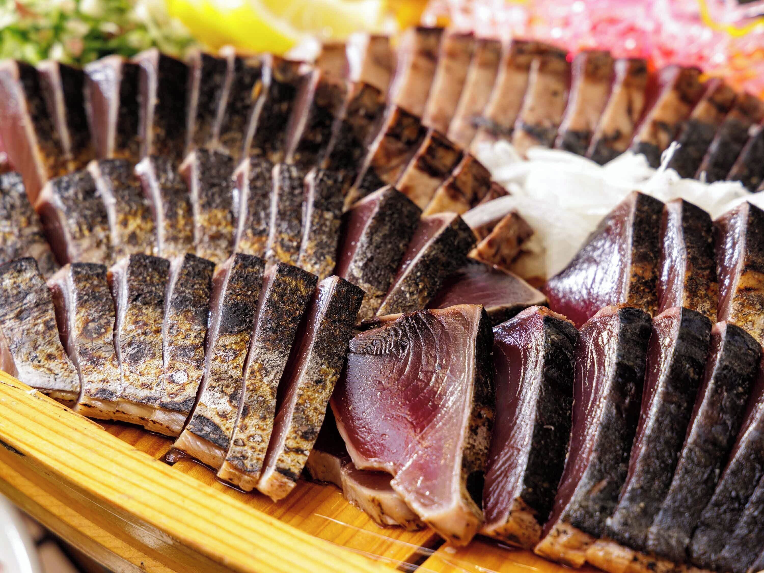 Une planche à découper en bois sur laquelle sont disposées des tranches de viande, probablement du porc, en forme d’éventail.