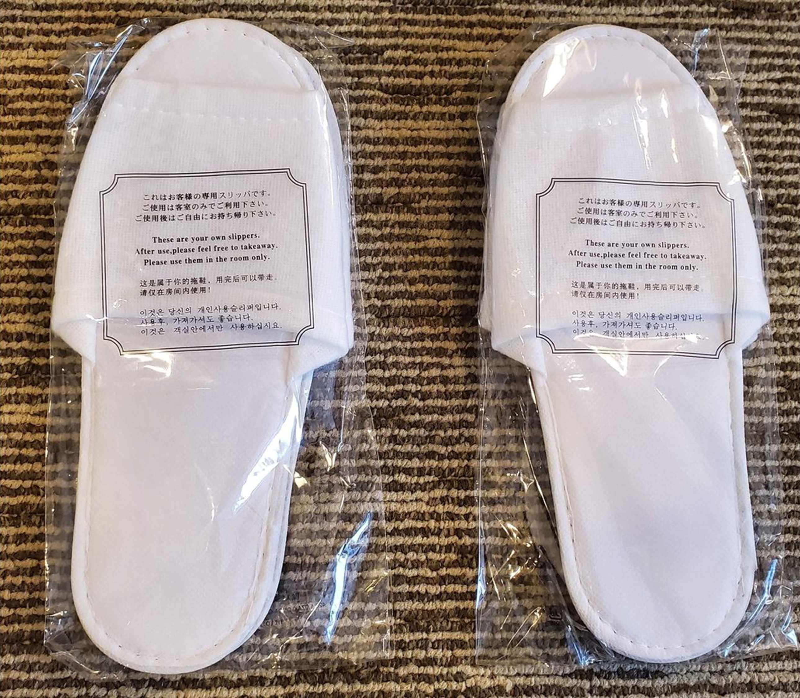 A pair of white slippers in plastic packaging with text in Japanese.