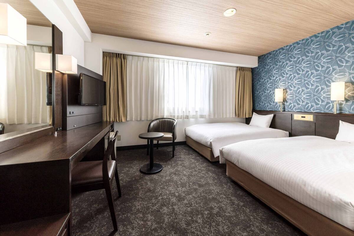 A hotel room with a bed, a desk, a chair, and a TV.