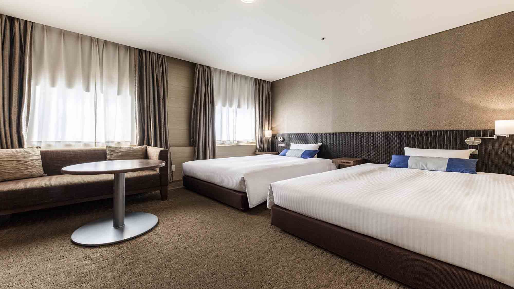 A hotel room with two beds, a sofa, a round table, and a large window with curtains.