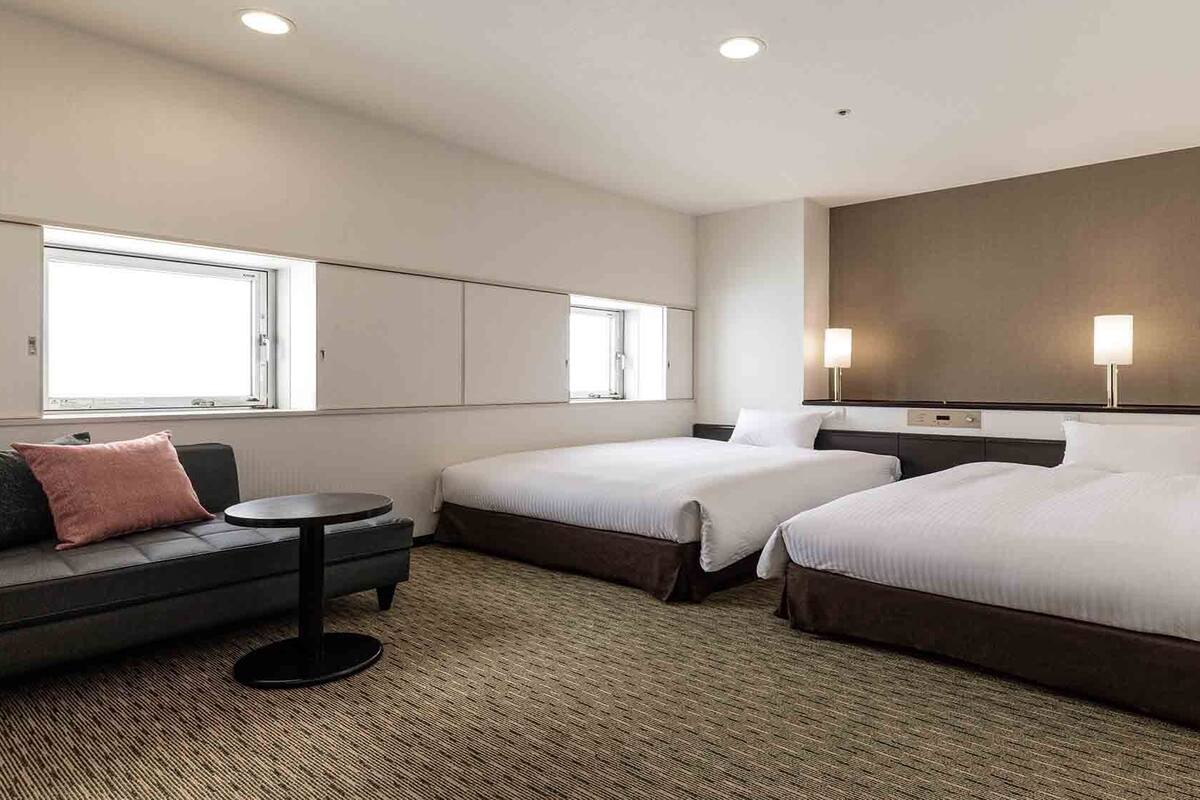 A hotel room with two beds, a sofa, a small table, and a large mirror.