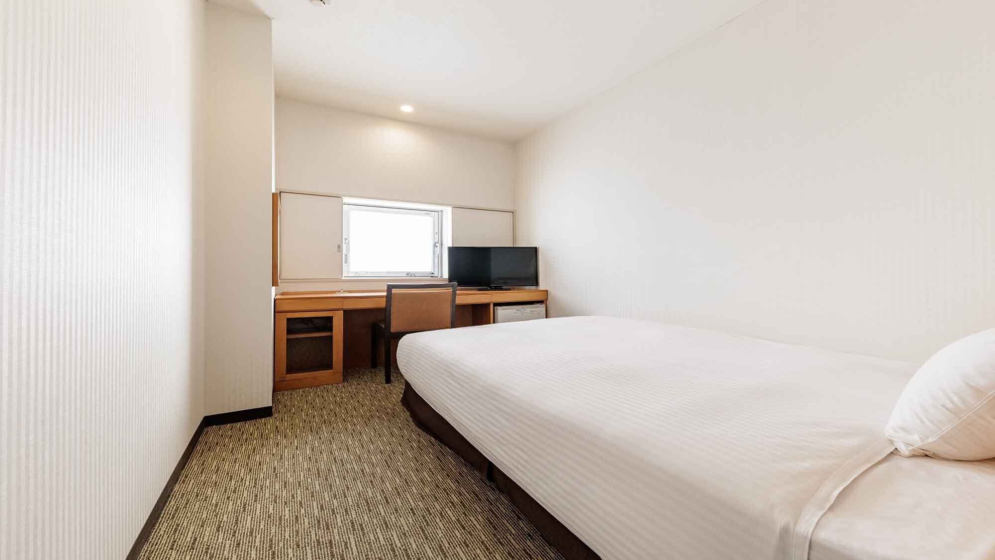 A hotel room with a bed, a desk with a television, and a window.