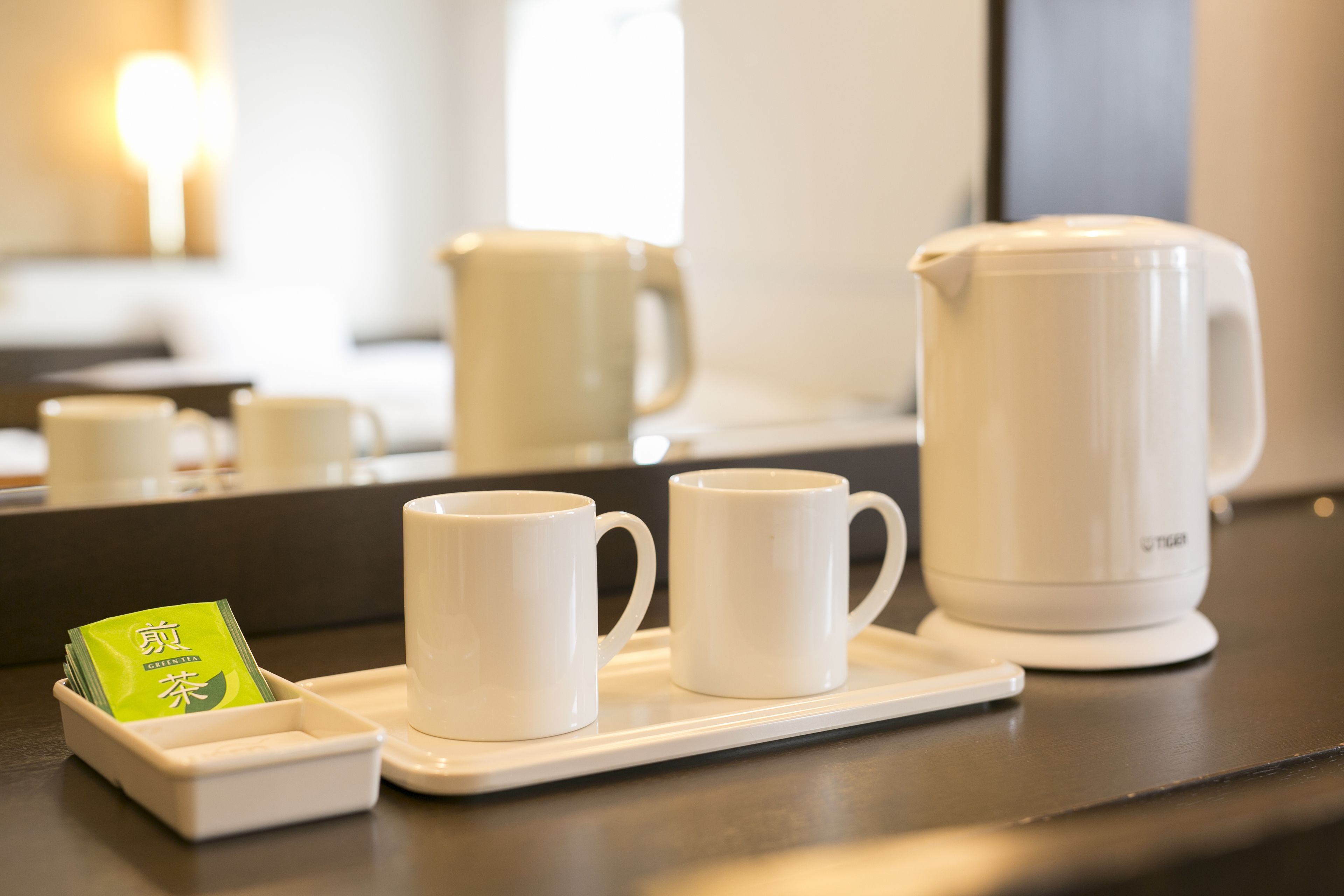 A tray with two white mugs and a white teapot on a dark countertop.