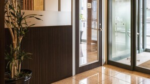 A modern lobby with a reception desk, a glass door entrance, and a potted plant. - Nishitetsu Inn Kurosaki (Kitakyushu)