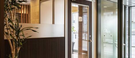Un vestíbulo moderno con mostrador de recepción, puerta de cristal y una planta en maceta.