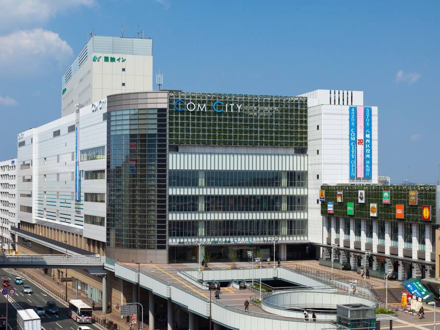 A modern building with a prominent "COM CITY" sign, featuring a glass facade and a covered pedestrian area.