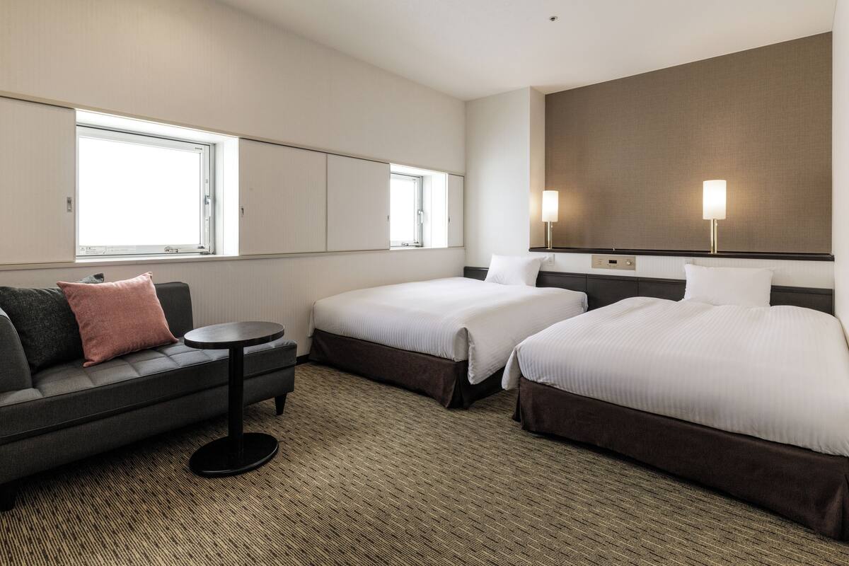 A hotel room with two beds, a sofa, a small table, and a large window.