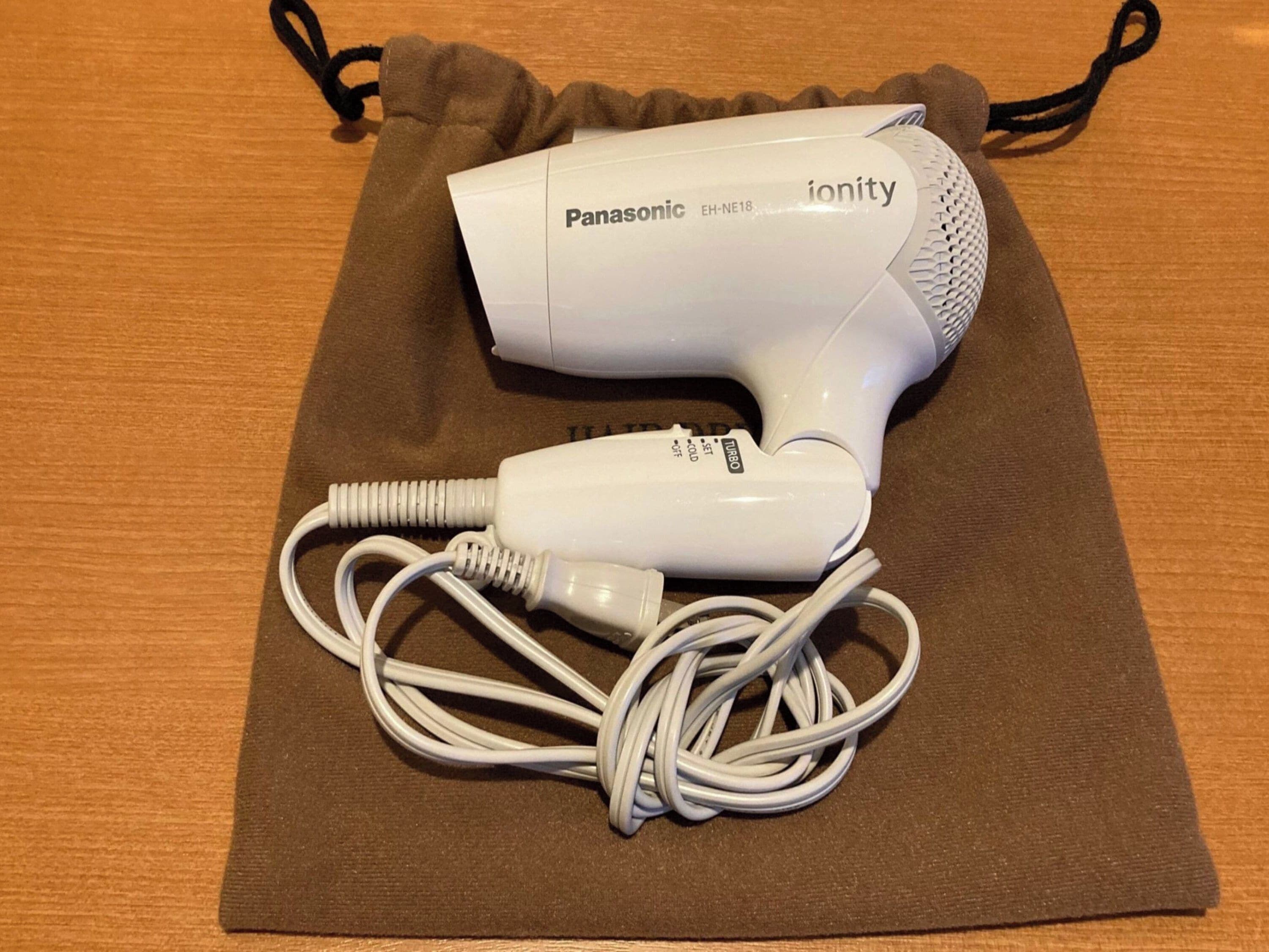 A Panasonic ionity hair dryer with a power cord, placed on a brown fabric surface.