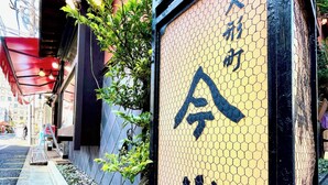 A building with a yellow and black sign featuring Chinese characters, a red awning, and a narrow sidewalk with a stone border. - Nishitetsu Inn Nihonbashi (Tokyo)