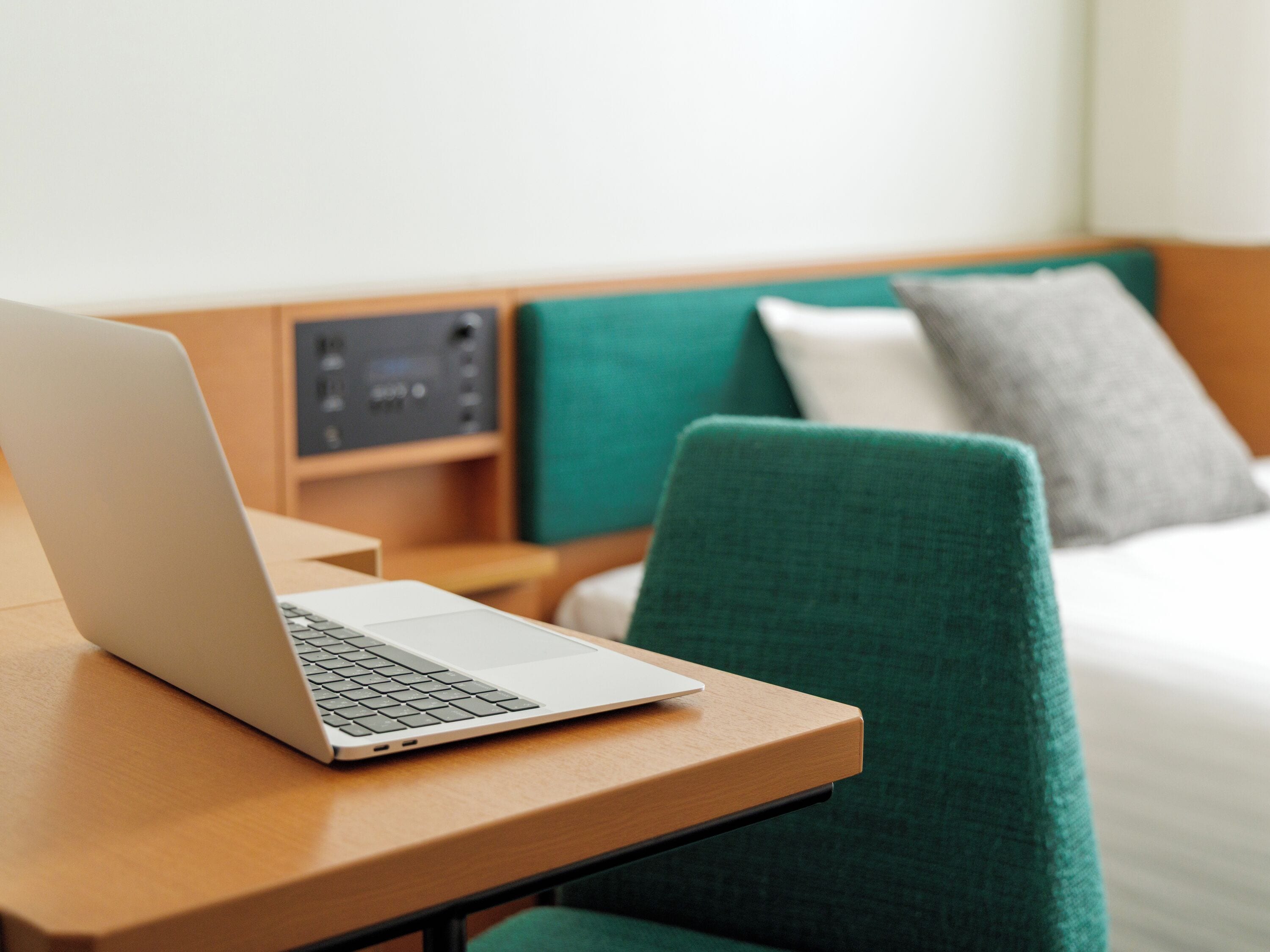 A hotel room with a bed, a green upholstered chair, a wooden nightstand, and a laptop on a wooden table.