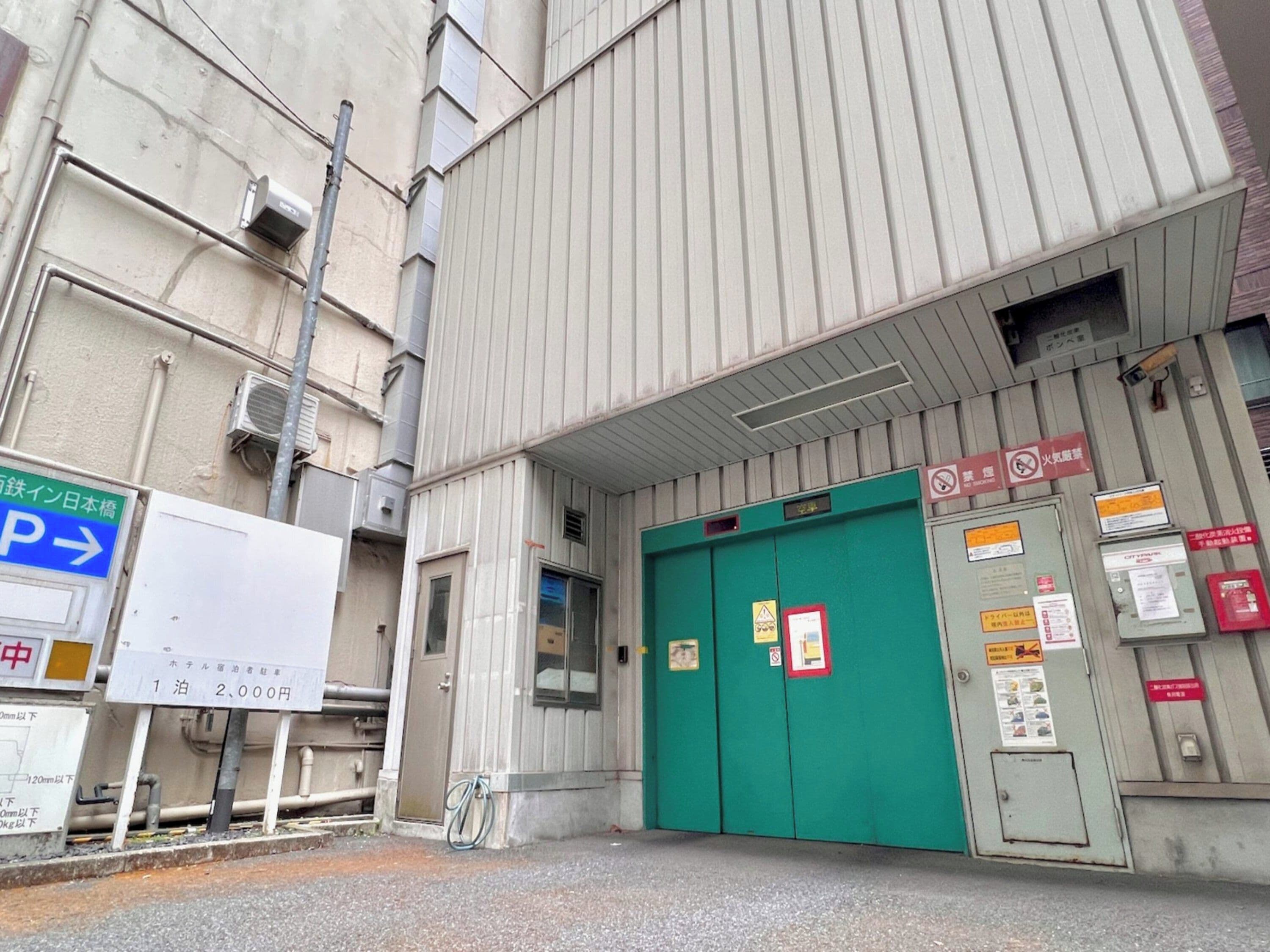 A building entrance with a green door, a parking sign, and various safety and informational signs.