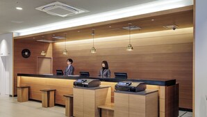 A reception desk with a wooden finish, two receptionists, a clock, and a security camera on the ceiling. - Nishitetsu Inn Nihonbashi (Tokyo)