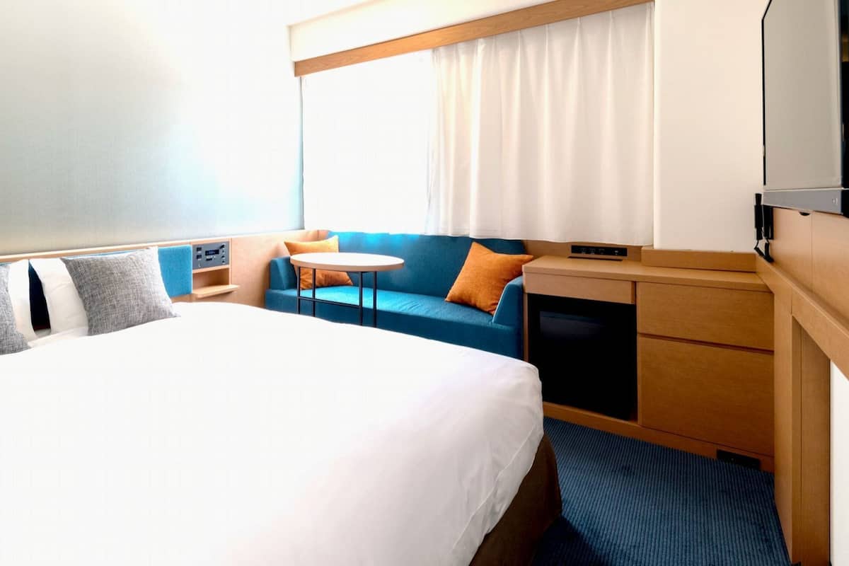 A hotel room with a large bed, a small table, a sofa, and a TV.