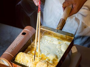 Iemand bereidt eten met een pan en een apparaat, mogelijk een keukenmachine, op een tafel.