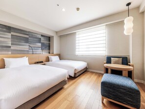 Een hotelkamer met twee bedden, een bureau, een stoel, een lamp en een groot raam met jaloezieën.