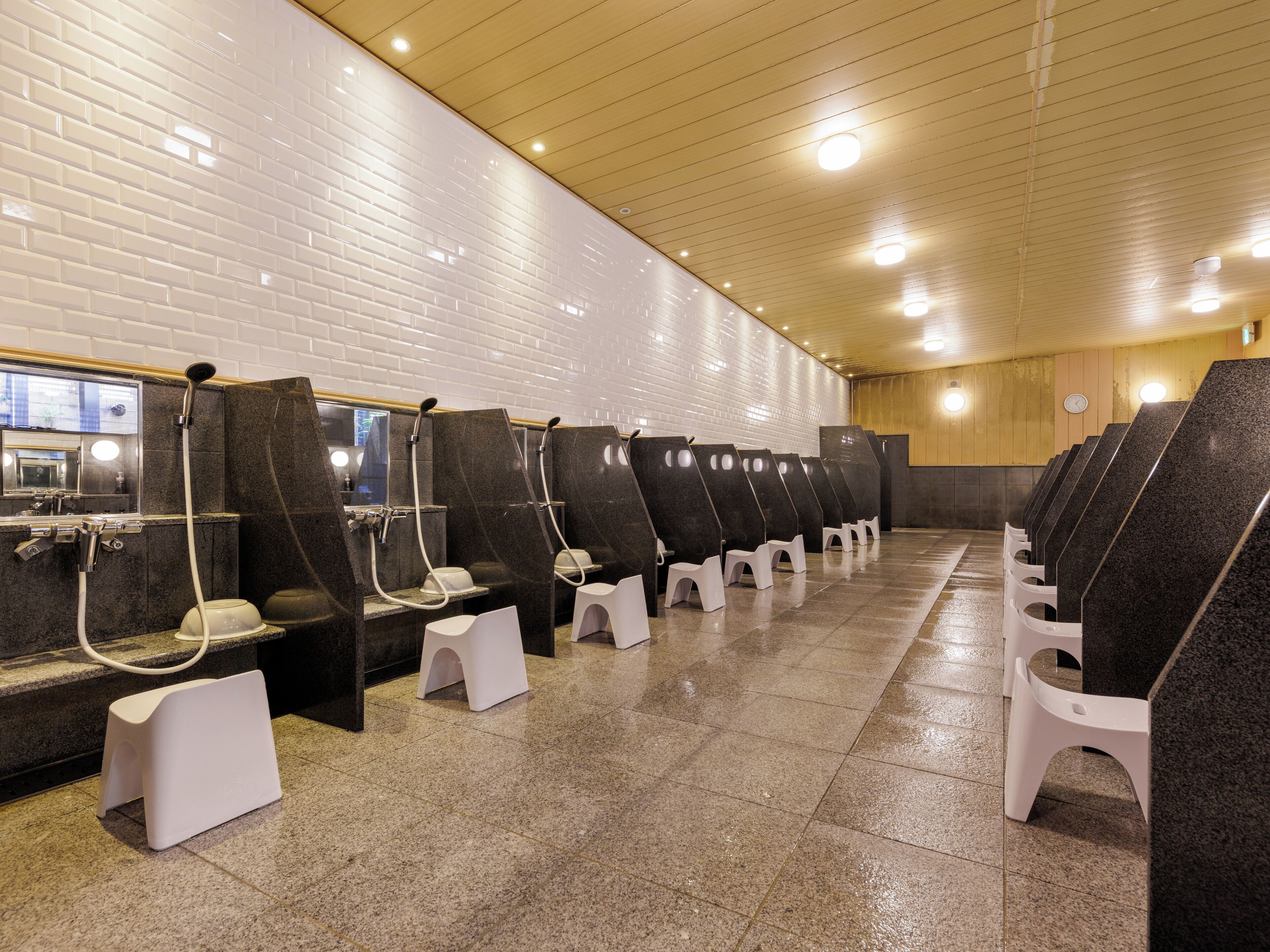 A row of individual shower cubicles with a tiled wall and wooden ceiling.
