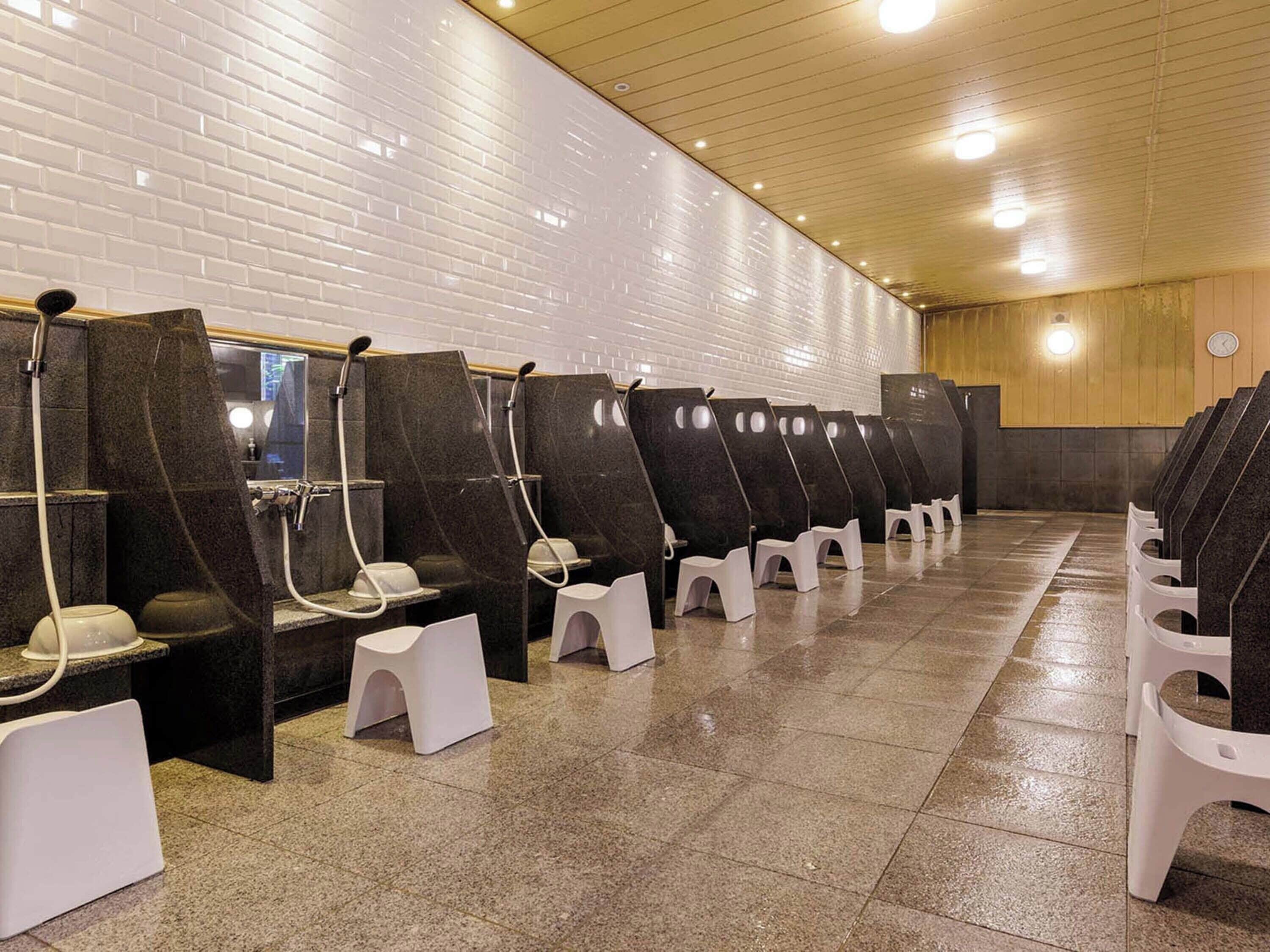 A row of individual shower cubicles with white stools, a tiled floor, and a wooden ceiling.