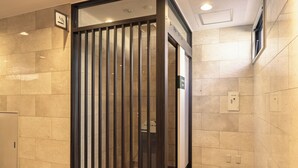 A modern elevator with a metal grille door, a sign indicating a smoking area, and a tiled floor. - Nishitetsu Inn Tenjin (Fukuoka)