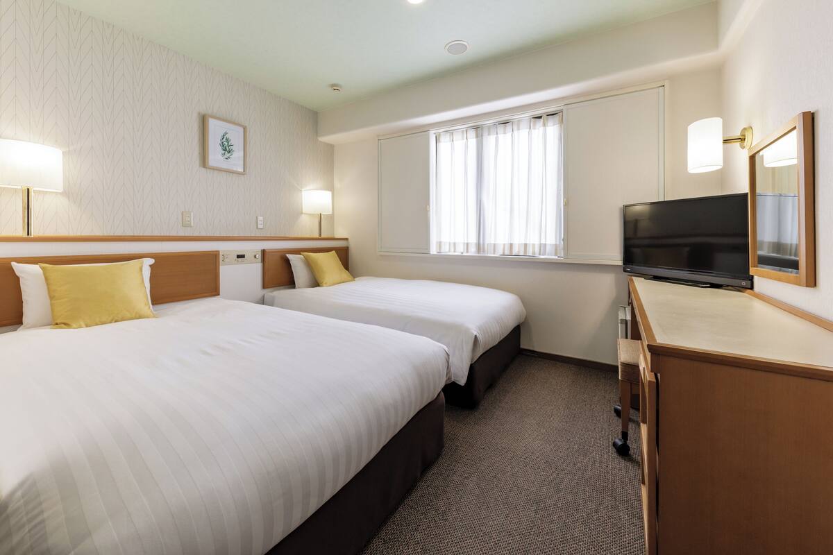A hotel room with two beds, a TV, and a window with curtains.