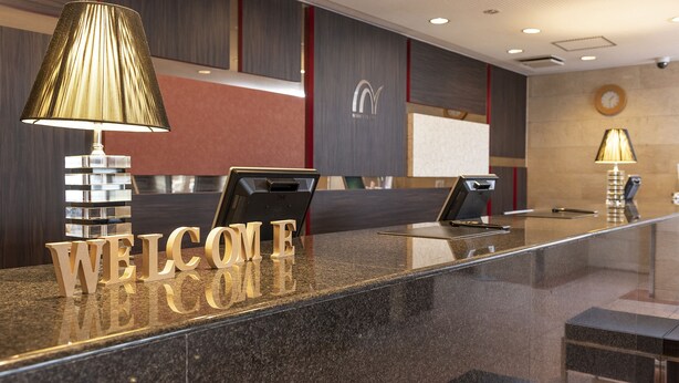 A reception desk with a "WELCOME" sign, a digital screen, and a lamp. - Nishitetsu Inn Tenjin (Fukuoka)