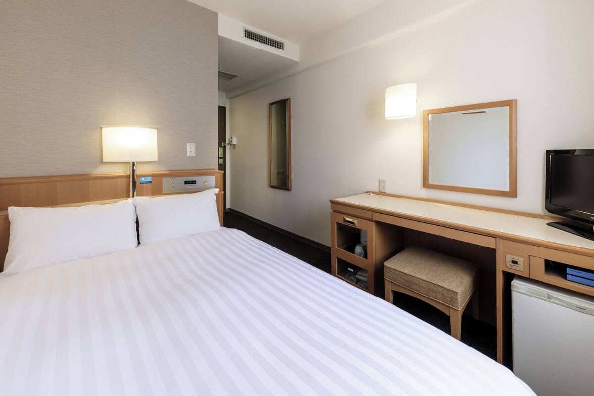 A hotel room with a large bed, a desk with a chair, a television, and a mirror.