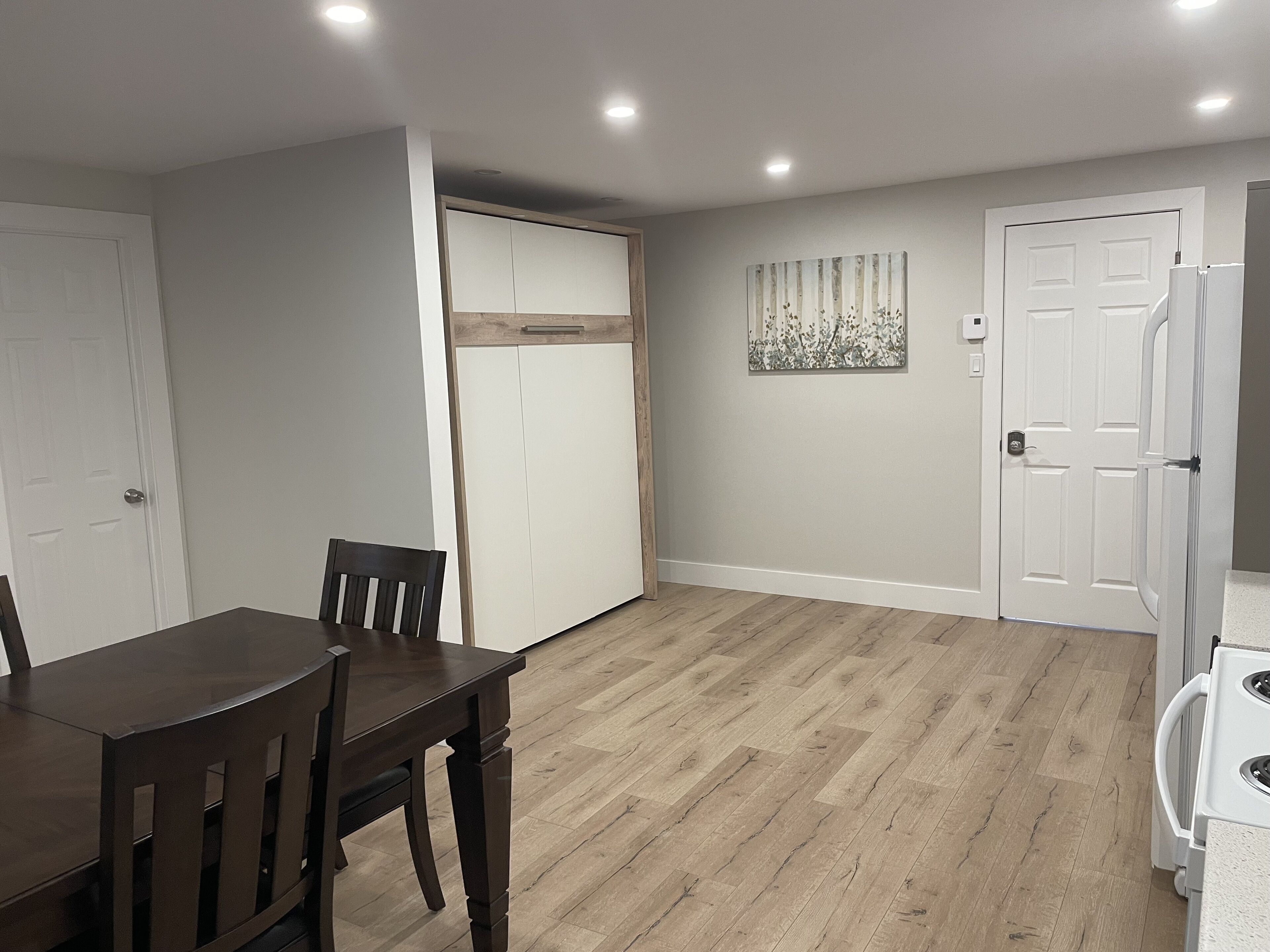 Un comedor con una mesa y sillas de madera, una puerta blanca, un armario blanco y una lámpara fijada a la pared.