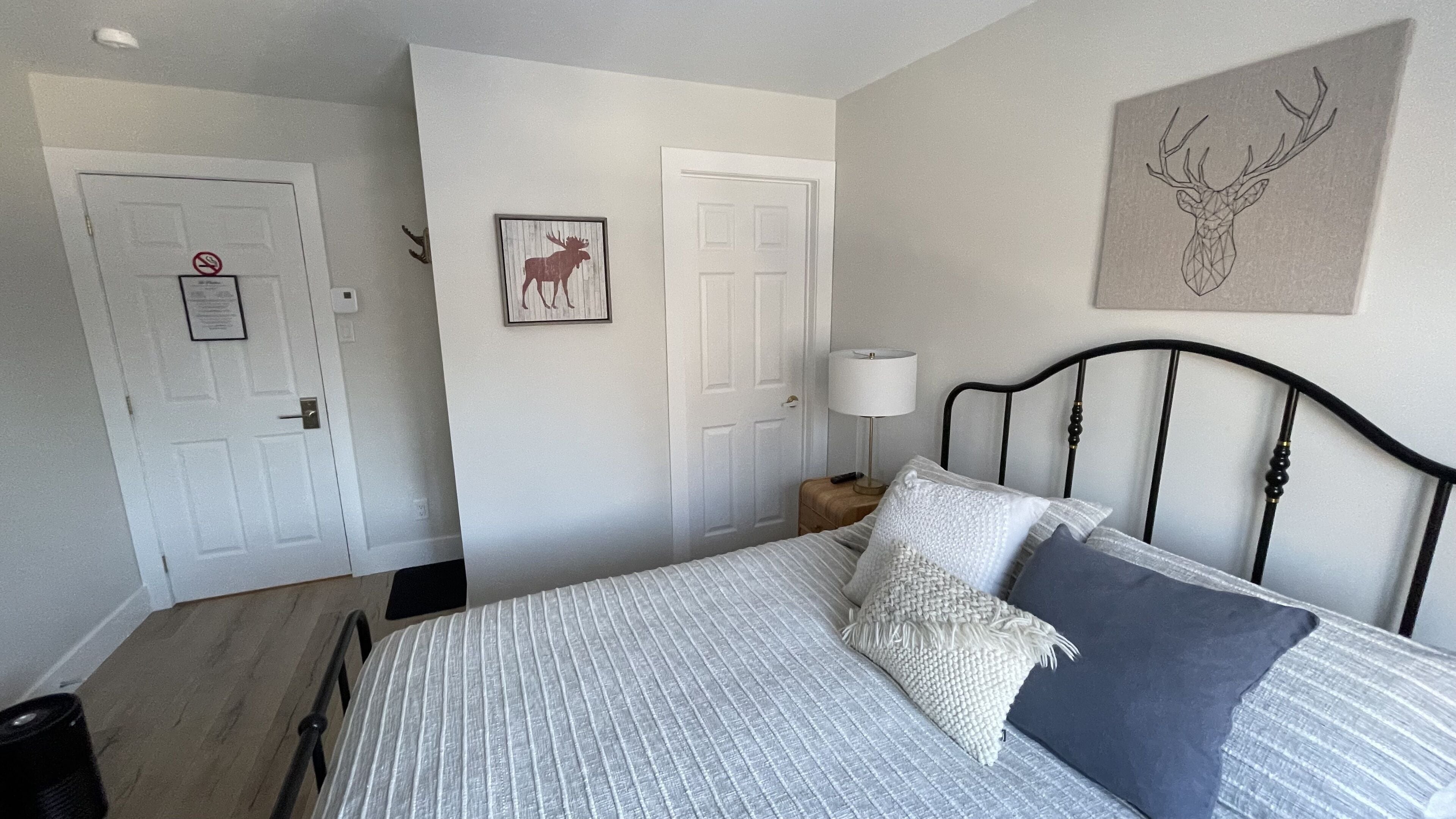 Un dormitorio con cama, almohadas, una mesita de noche, una lámpara y dos puertas.