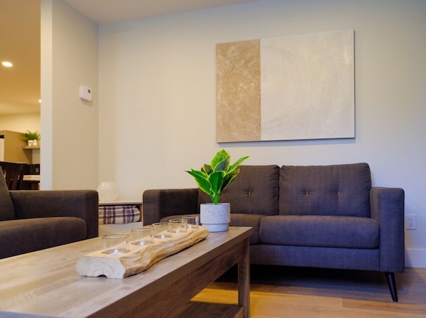 Een moderne woonkamer met een grijze bank, een houten salontafel en een potplant.