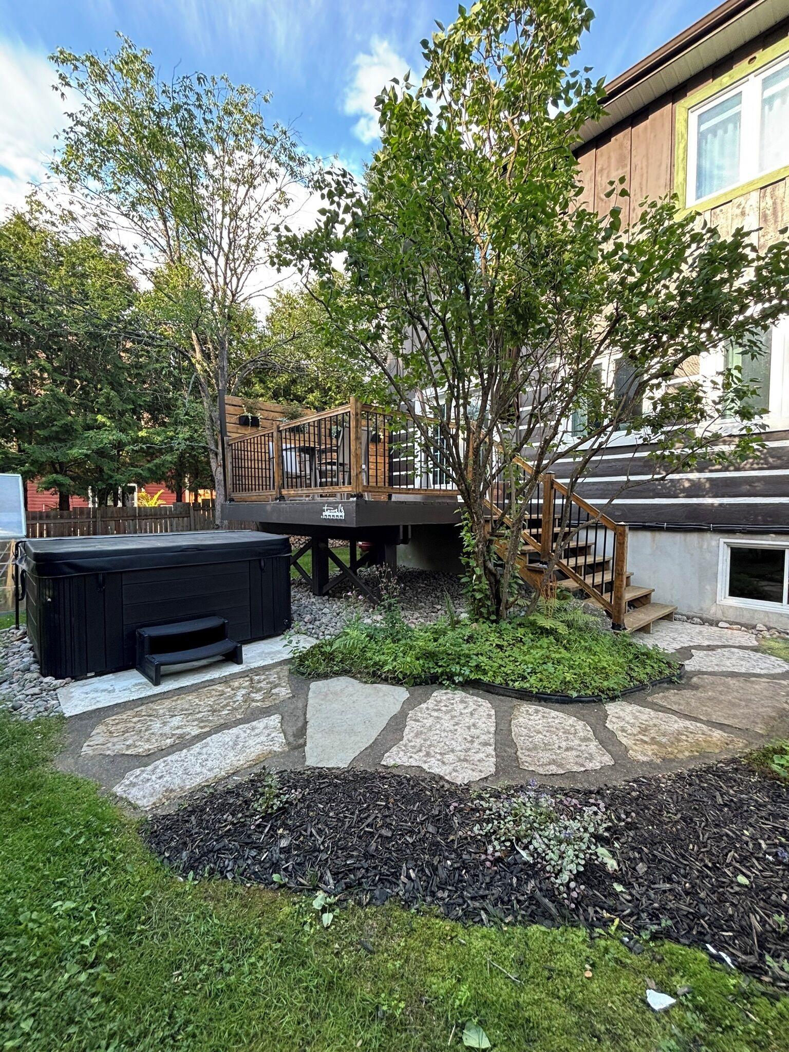 A backyard with a hot tub, stone pathway, and a wooden deck.