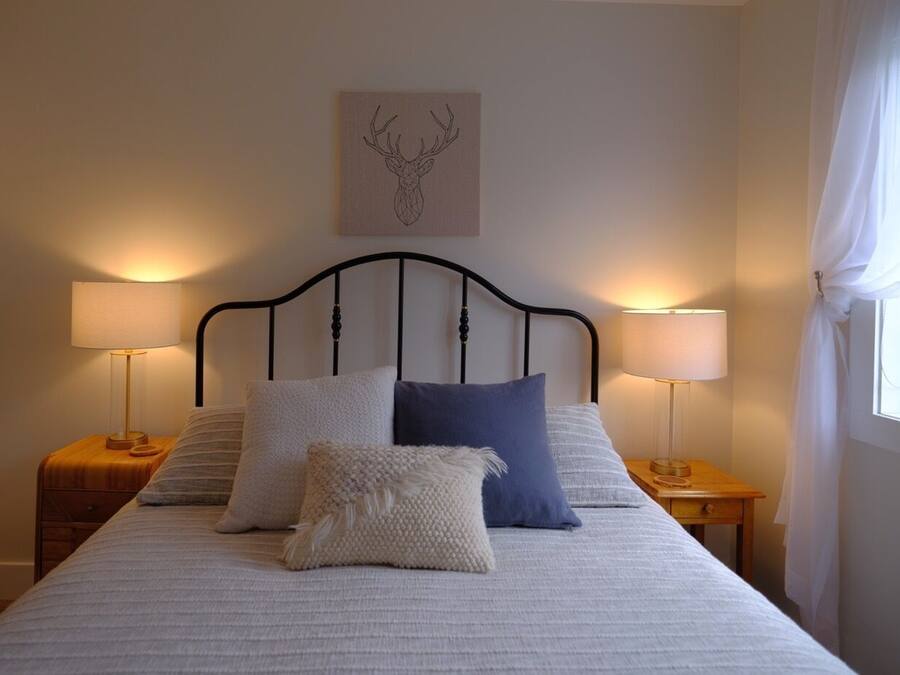 Ein ordentlich bezogenes Bett mit Kopfteil, zwei Nachttische mit Lampen und ein Wandbild mit Hirschgeweih.