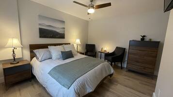 A neatly arranged bedroom with a bed, two bedside tables with lamps, a chair, a desk, and a ceiling fan.