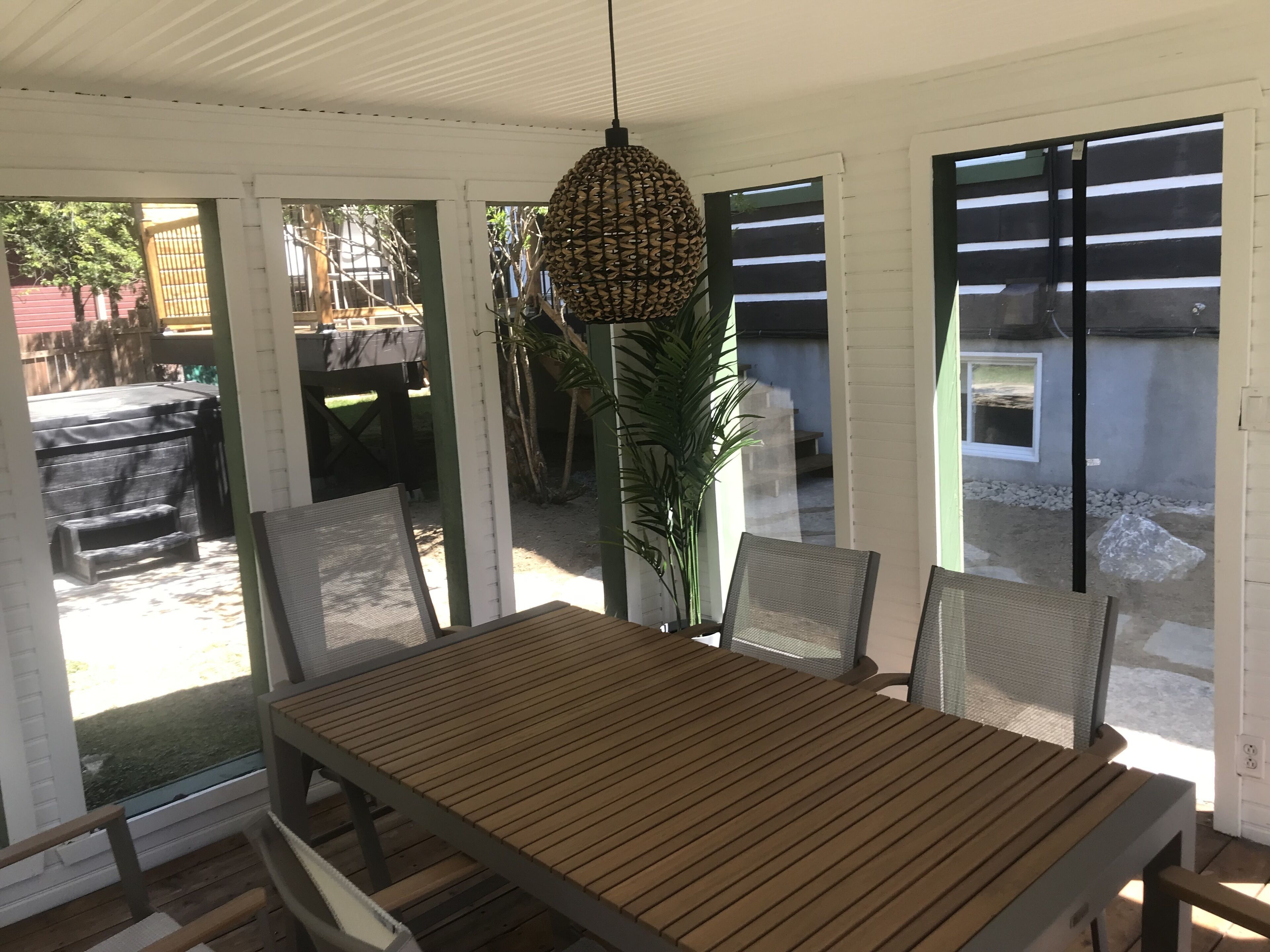 An outdoor patio with a wooden table and chairs, a hanging light fixture, and a view of the backyard.